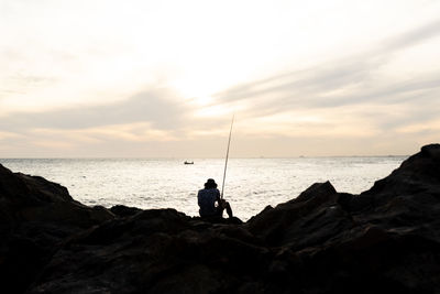 Silhouette of a fisherman with fishing rod sitting on the rocks of the rio vermelho beach