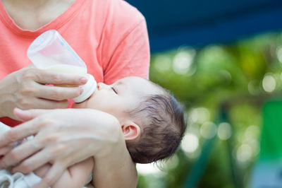 Midsection of mother feeding milk to daughter outdoors