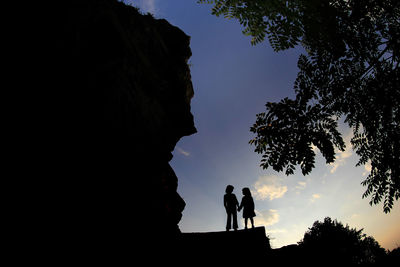 Low angle view of silhouette people on rock against sky