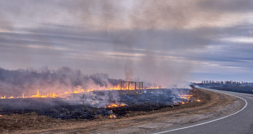 In the spring in the evening, dry grass burns on the field near the road. grassroots natural fire.