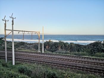 Railroad tracks by sea against clear sky