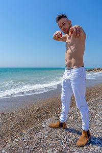 Full length of shirtless man standing at beach against sky