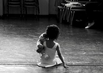 Rear view of girl with teddy bear sitting on floor at ballet studio