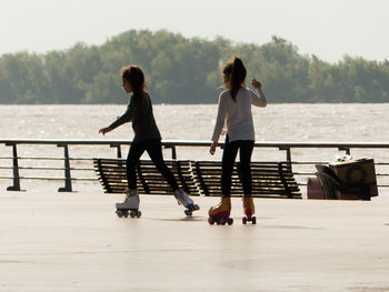 Girls roller skating on footpath against lake