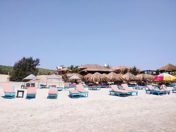 Thatched roof hut and parasols at beach against clear sky
