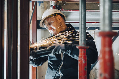 Male construction worker cutting metal with machinery at site