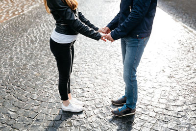 Low section of couple holding hands while standing on cobblestoned footpath