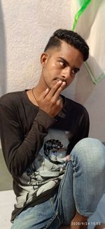 Portrait of young man looking away while sitting against wall