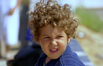 Close-up of thoughtful boy with curly brown hair sitting outdoors