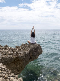 Rear view of woman meditation on rock against sea