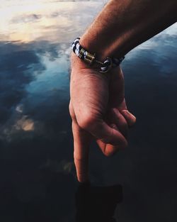 Cropped hand of man touching lake during sunset