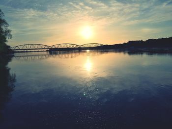 Silhouette bridge over river against sky during sunset