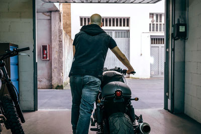 Rear view of man with motorcycle in garage