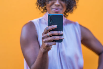 Midsection of woman using smart phone standing against yellow background