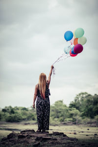 Rear view of woman with balloons standing on field