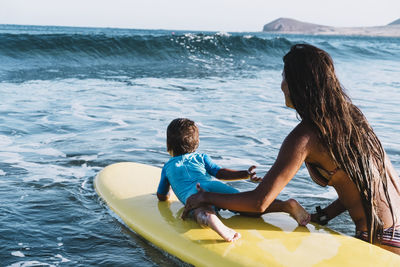 Young mother and son paddle on a surfboard at sea