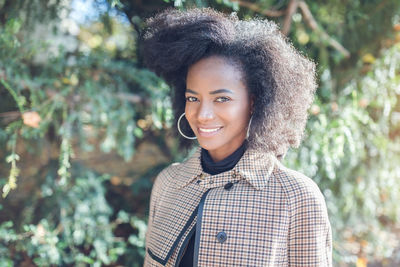 Portrait of smiling young woman standing against trees