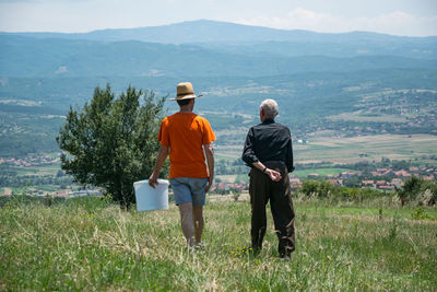 Rear view of friends standing on field against mountains