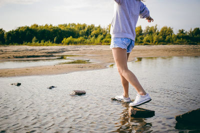 Low section of woman balancing on rocks at beach against sky