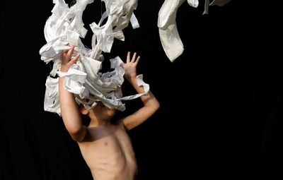 Shirtless boy throwing clothes while standing against black background