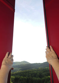 Low section of person hand holding window against sky