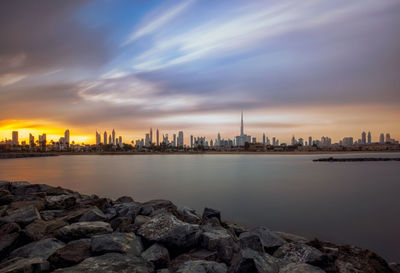 Sea by buildings against sky during sunset