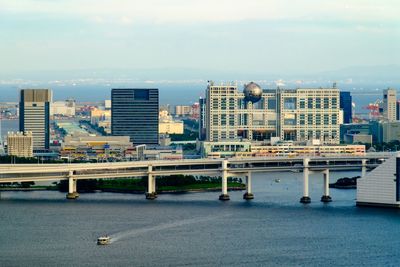 Bridge over river by fuji television building against sky