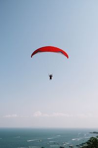 Low angle view of man paragliding over sea against clear sky