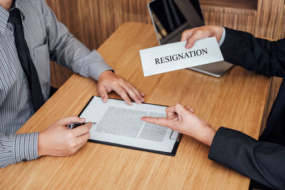 Manager holding resignation text and employee signing the document in office