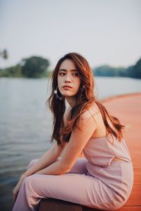 Side view of thoughtful young woman sitting by lake