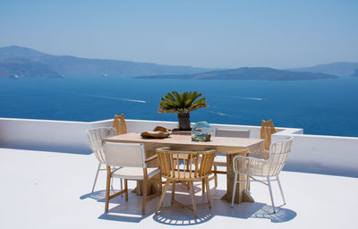 Furniture composed by a table and some chairs on a white terrace of a house in santorini greece where you can enjoy meal while seeing a romantic seascape to the blue aegean sea. horizontal ph