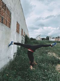 Woman doing handstand by wall against sky