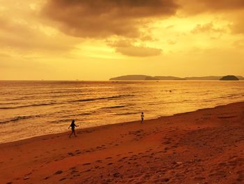 Silhouette people on beach against sky during sunset