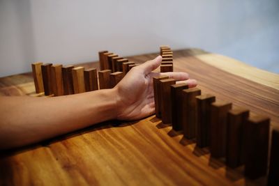 Cropped hand of person blocking wooden dominoes on table