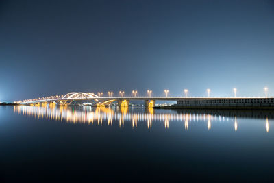 Illuminated bridge over river against sky at night