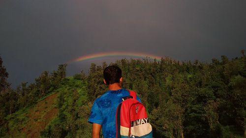 Rear view of man standing against rainbow in sky