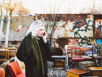 Side view of woman talking on smart phone surrounded by chairs in flea market