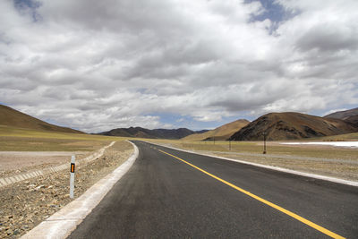 A flat, newly built wide asphalt road leads to the beautiful mountains in the distance