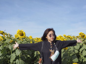 Portrait of young woman standing by sunflower against sky