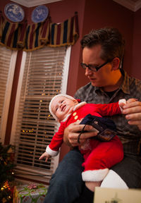 Father with baby boy wearing santa costume at home