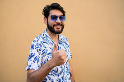 Portrait of young man wearing sunglasses standing against wall