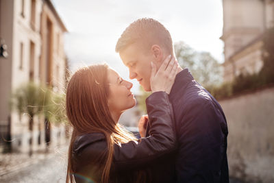 Couple looking at each other while standing amidst buildings against sky