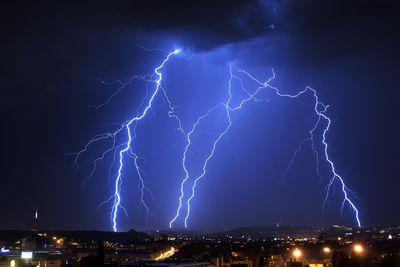 Lightning over illuminated cityscape against sky at night