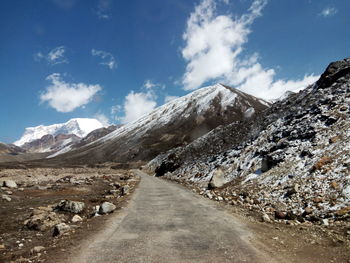 Empty country road leading towards mountains against blue sky