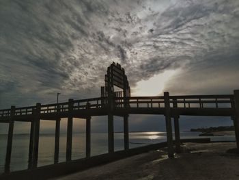 Silhouette bridge over sea against sky at sunset