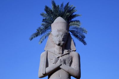 Low angle view of statue against blue sky with palm tree