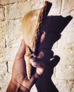 Cropped hand holding ice cream cone against wall