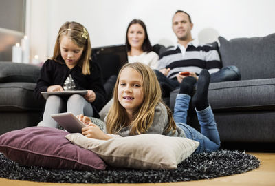 Portrait of girl holding digital tablet with family in living room