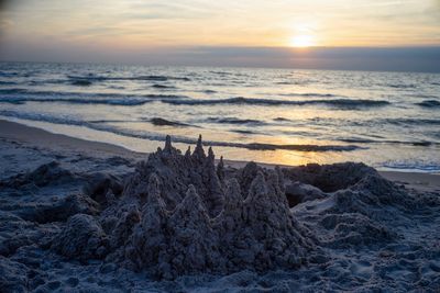 Scenic view of sea with sandcastle against sky during sunset