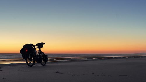 Silhouette people riding motorcycle on beach against clear sky during sunset